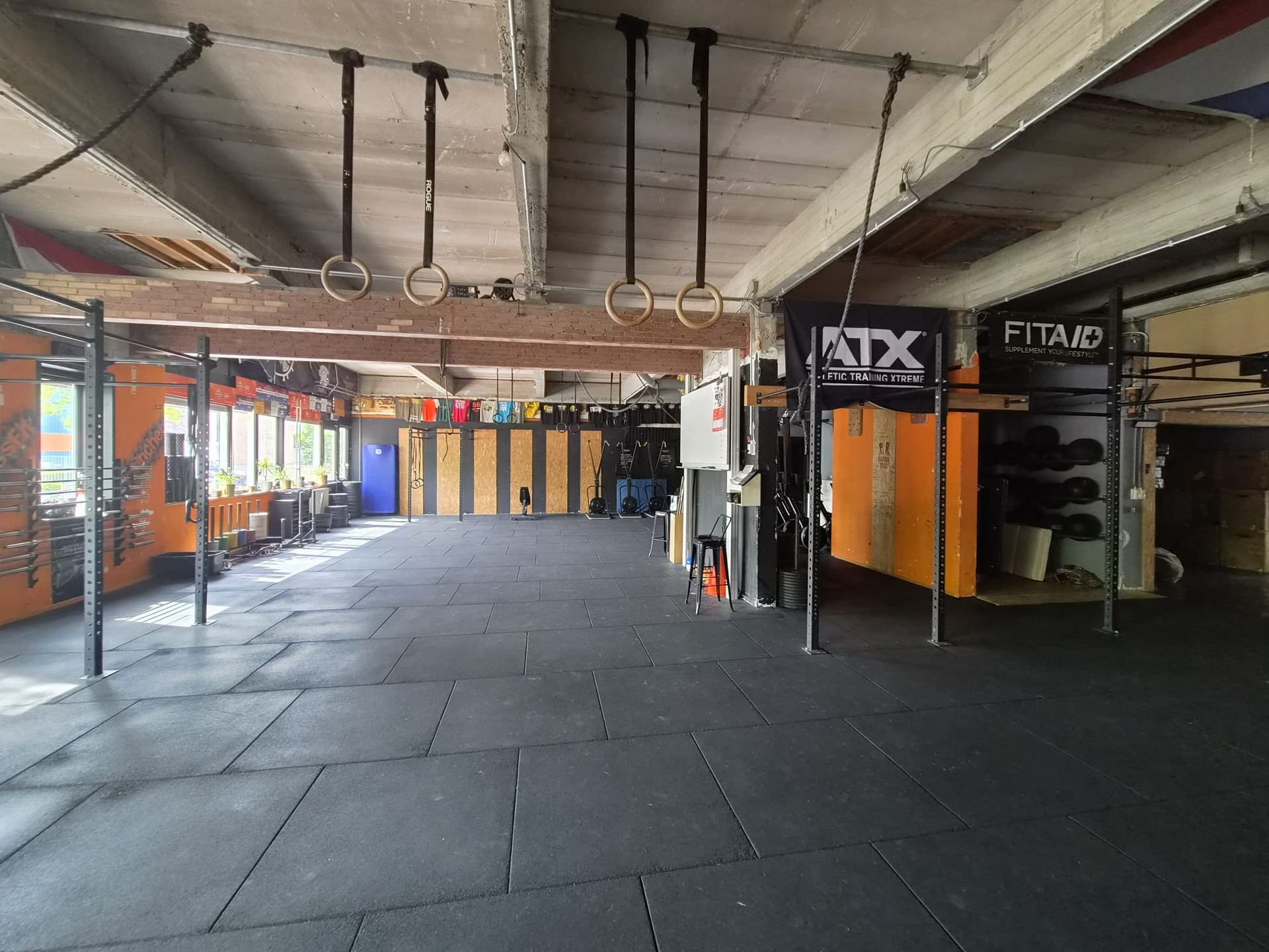 De lege trainingsvloer van CrossFit Gorinchem met ringen, rigs en oranje houten wanden